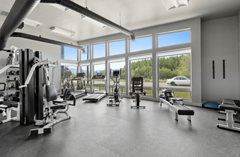 A spacious gym with a variety of equipment and a view of the outdoors through large windows.